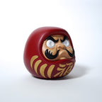 Modern red Japanese Daruma doll in resin, three quarter side view on white background