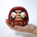 Hand holding a medium sized red Japanese Daruma doll to show scale
