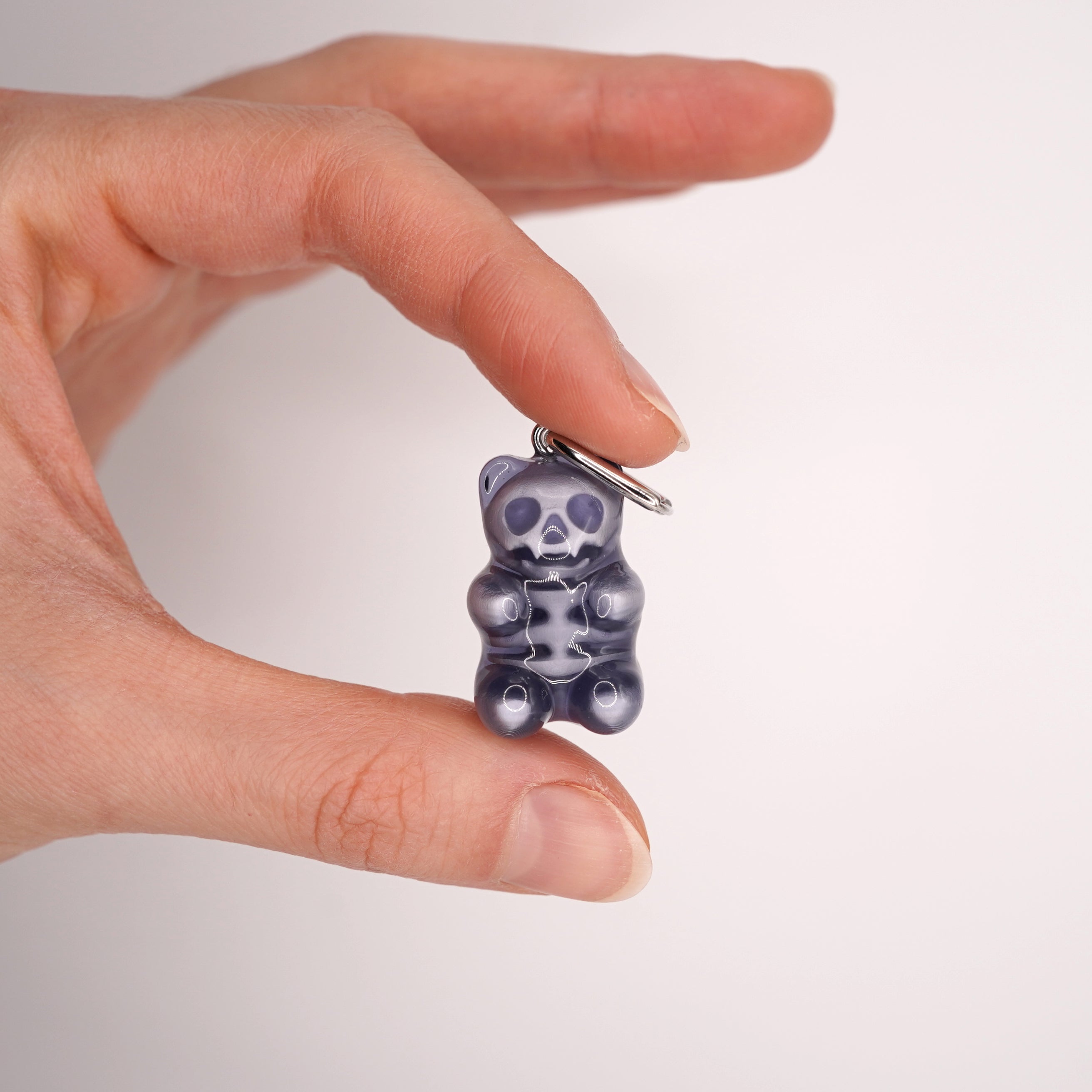 Close-up of transparent resin gummy bear skeleton earring, glossy handmade skull bear charm, dark aesthetic gothic candy jewelry