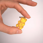 Close-up of yellow gummy bear skeleton earring held in fingers, transparent resin with internal bones