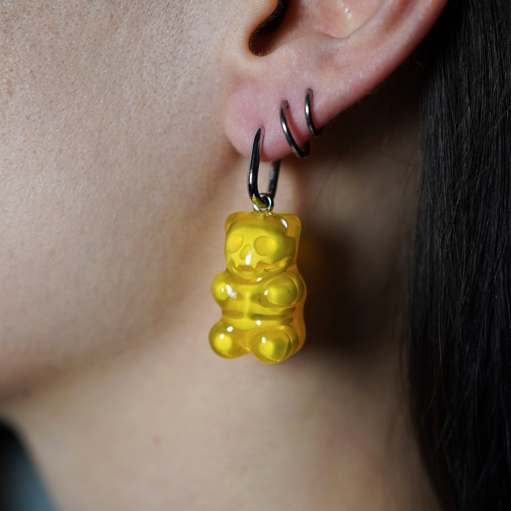 Yellow transparent gummy bear skeleton earring worn on ear, cute creepy resin jewelry with visible skull