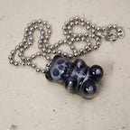 Black resin gummy bear skull pendant lying on stone background with silver ball chain, high-contrast X-ray skeleton effect.