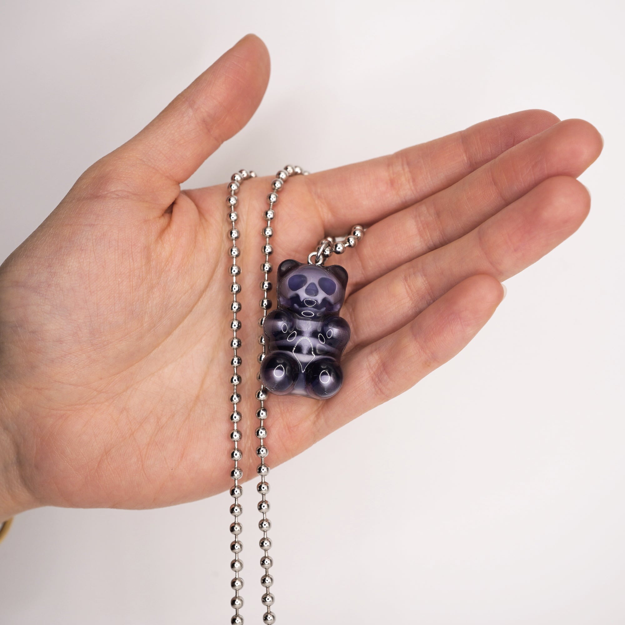 Black X-ray gummy bear pendant shown in hand for scale, glossy resin finish with visible white skeleton, silver ball chain necklace.