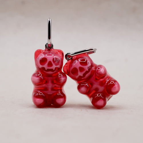 Close-up of a translucent red gummy bear earring revealing a detailed internal skeleton, gothic chic jewelry style.
