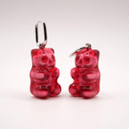 Pair of translucent red skeleton gummy bear earrings on a white background, 3D printed alternative wearable art.