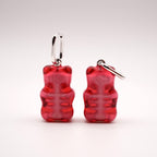 Two pairs of red gummy bear-shaped earrings with silver-colored hoops. The earrings have a translucent appearance, with a lighter pink interior. The earrings are displayed against a white background.
