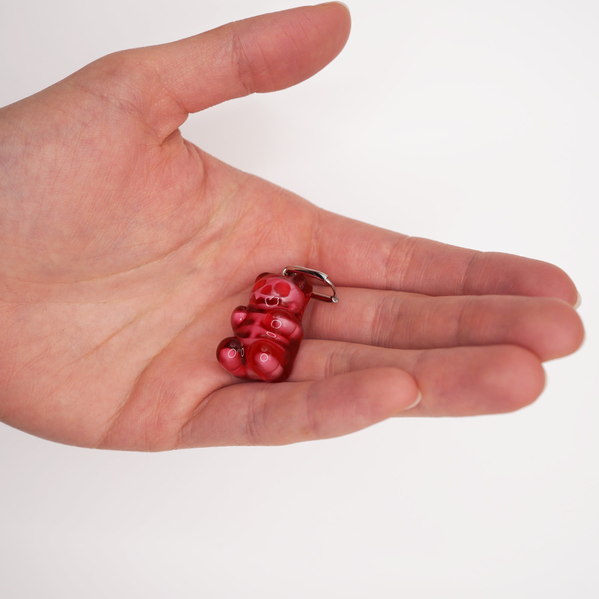 Close-up detail of the transparent red resin and anatomical skeleton design of the gummy bear earring resting in the palm of a hand.