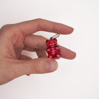 Alternative luxury skeleton bear earring held between fingers to show its small scale and the high clarity of the red resin.