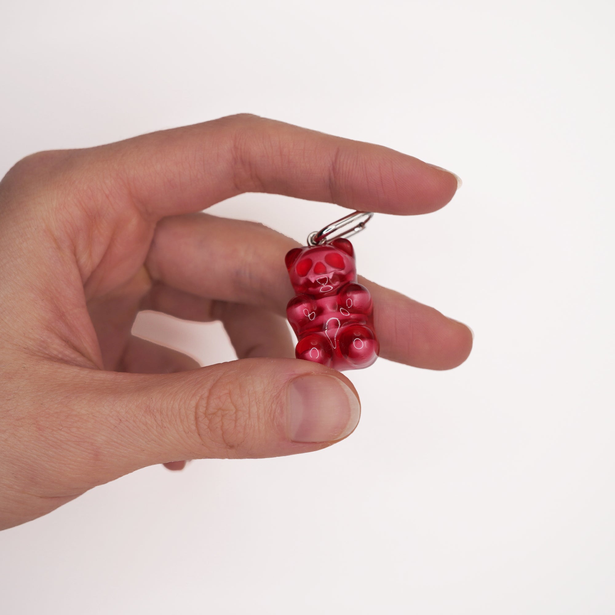 Alternative luxury skeleton bear earring held between fingers to show its small scale and the high clarity of the red resin.