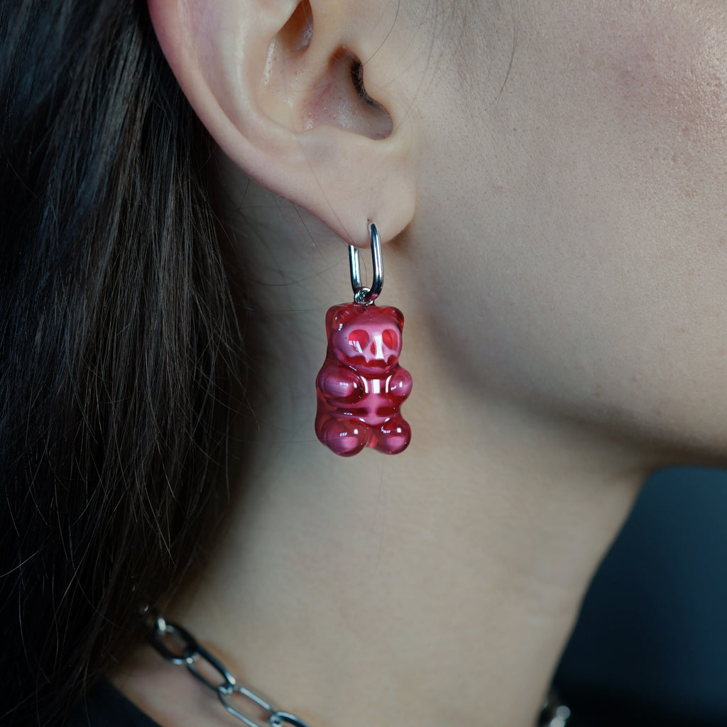 Translucent red skeleton gummy bear earring worn on the ear, attached by an elegant hypoallergenic surgical steel hoop.