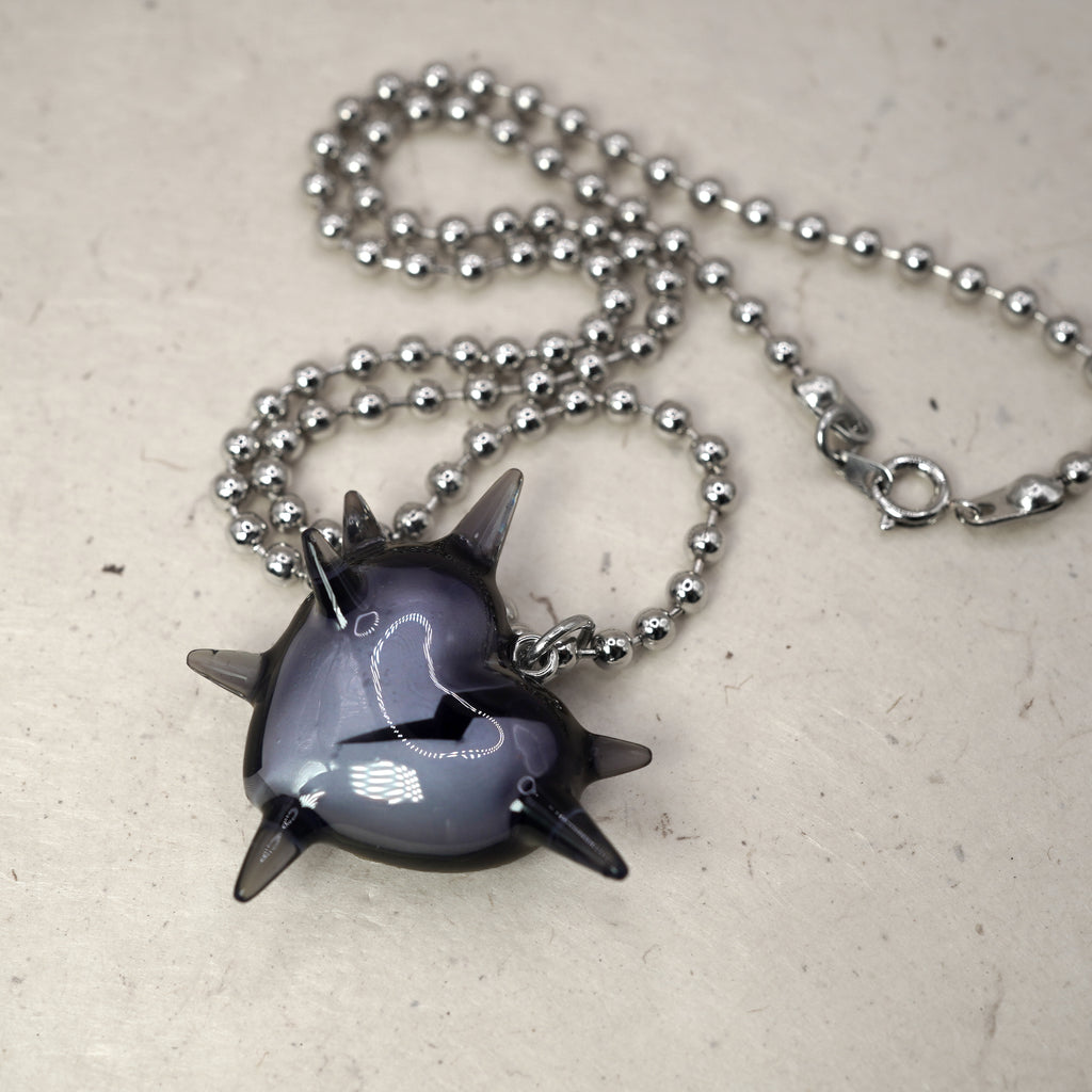 Close-up of glossy spiked heart charm with cracked heart insert, transparent black resin pendant on rhodium plated chain